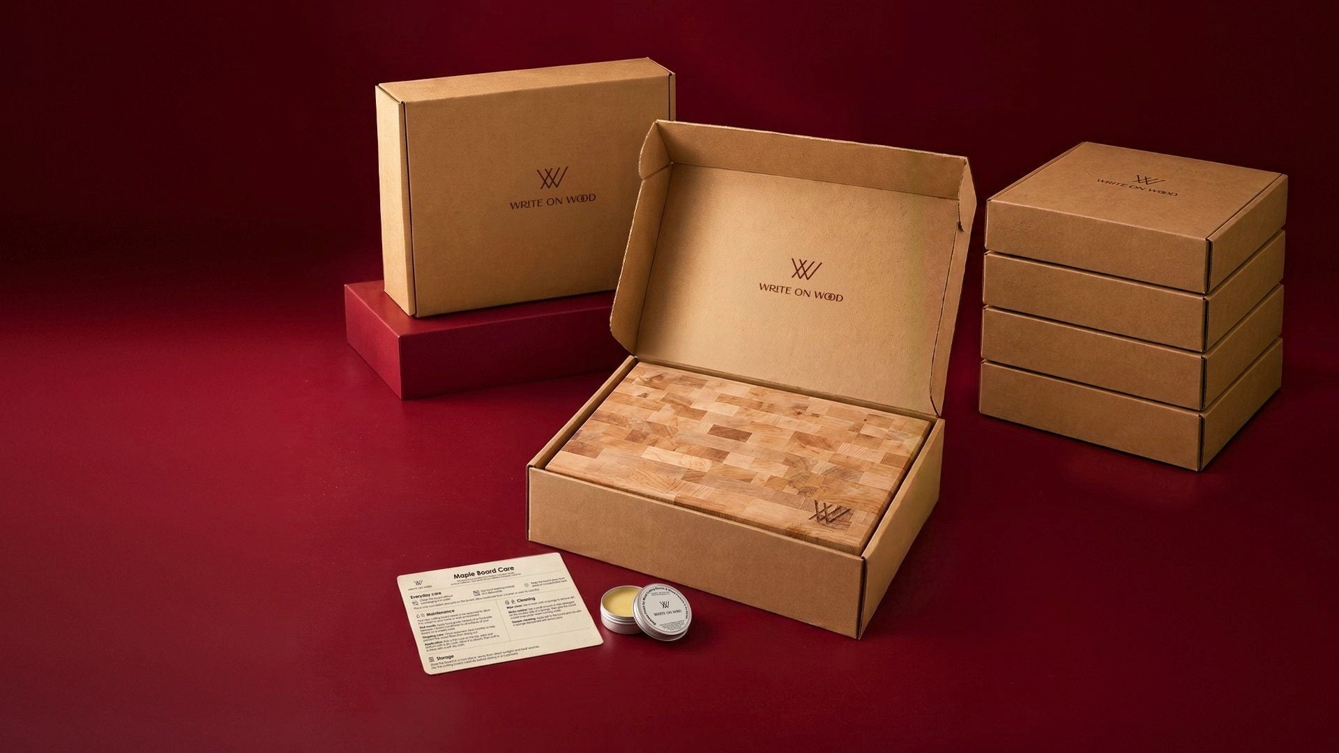 A hardwood board in an open Write On Wood gift box, with a care card, beeswax tin and stacked gift boxes